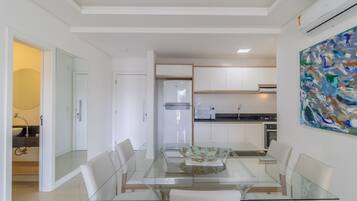 A modern kitchen with white cabinets, a glass dining table, and a contemporary painting on the wall.