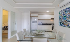 Uma cozinha moderna com armários brancos, uma mesa de jantar de vidro e uma pintura contemporânea na parede.