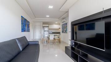 A modern living room with a large flat-screen TV, a grey sofa, and artwork on the walls.