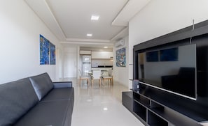 Uma sala de estar moderna com uma televisão de tela grande, um sofá cinza e obras de arte nas paredes.