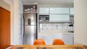 A modern kitchen with a stainless steel refrigerator, a microwave, and a gas stove. There are two orange chairs at a wooden table. - Apt w/ Balcony & BBQ 450m From the sea Reh0203 (Florianópolis)