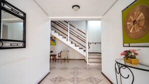 A hallway with a tiled floor, a staircase, a mirror, a wall-mounted decorative piece, and a small table with a potted plant. - Apt w/ Balcony & BBQ 450m From the sea Reh0203 (Florianópolis)
