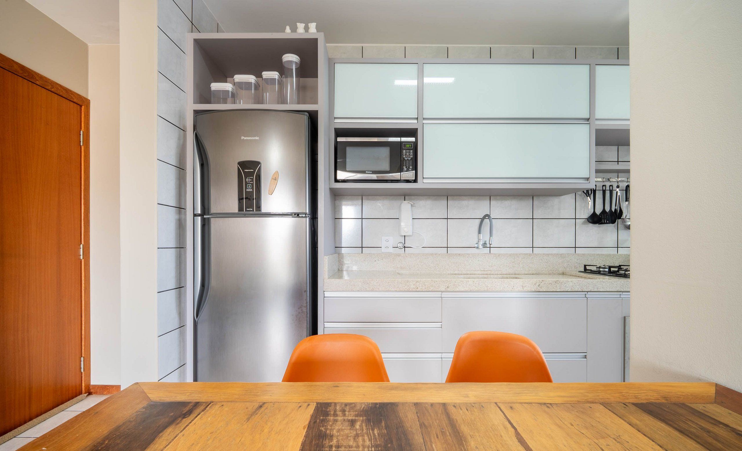 Una cocina moderna con un refrigerador de acero inoxidable, un microondas y una estufa a gas. Hay dos sillas naranjas junto a una mesa de madera.