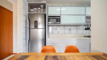 Una cocina moderna con un refrigerador de acero inoxidable, un microondas y una estufa a gas. Hay dos sillas naranjas junto a una mesa de madera.