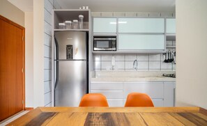 A modern kitchen with a stainless steel refrigerator, a microwave, and a gas stove. There are two orange chairs at a wooden table. - Apt w/ Balcony & BBQ 450m From the sea Reh0203 (Florianópolis)