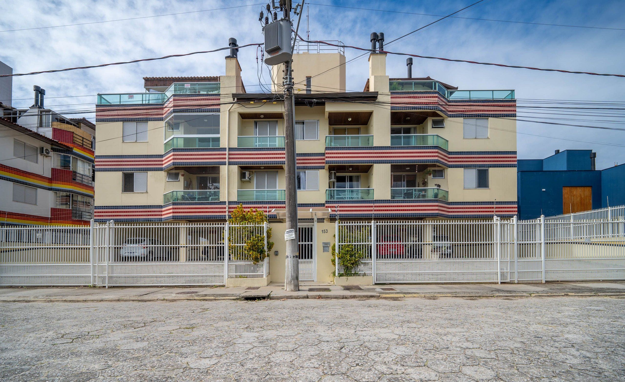 Un edificio residencial de varios pisos con balcones, una entrada porticada y una calle pavimentada.