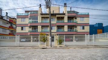 Un edificio residencial de varios pisos con balcones, una entrada porticada y una calle pavimentada.