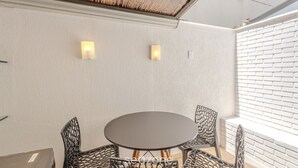Une pièce avec une table ronde et quatre chaises, deux lampes fixées au mur, un mur en briques blanches et un plafond à motifs.