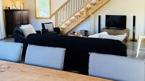 A spacious living room with a wooden staircase, a sofa set, a TV, and a wooden dining table. - LE GARAGE 17 (Frelighsburg)