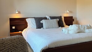 A bedroom with a wooden ceiling, a large bed with white bedding, two bedside tables with lamps, and a dark headboard. - LE GARAGE 17 (Frelighsburg)