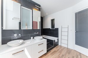 A modern bathroom with two sinks, a large mirror, and a bathtub.