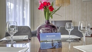 Ein Esstisch mit weißen Tellern, Besteck und Weingläsern, eine Vase mit rosa Blumen und ein Schild mit der Aufschrift 'Bassin d'Arcachon'.