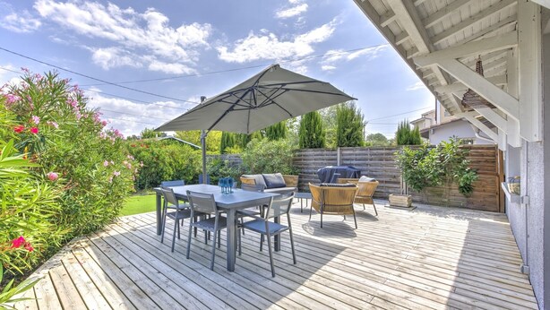 Eine Holzterrasse mit Tisch und Stühlen, einem großen Sonnenschirm und einer Grillgelegenheit.