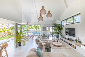 A modern living room with a large sofa, a TV, and a dining area with a bench and table. - Villa del Sol -  Villa contemporaine avec piscine, spa - un écrin de détente au Pays Basque (Anglet)