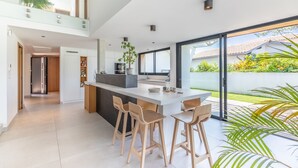 A modern kitchen with a central island, bar stools, and a large sliding glass door leading to a garden.