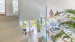A spacious living area with a glass staircase, a dining area, and a view of the outdoor garden.