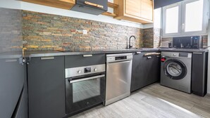 A modern kitchen with a stone backsplash, stainless steel appliances, and wooden cabinets. - L’Escapade du Quai - Proche Gare (Pontivy)
