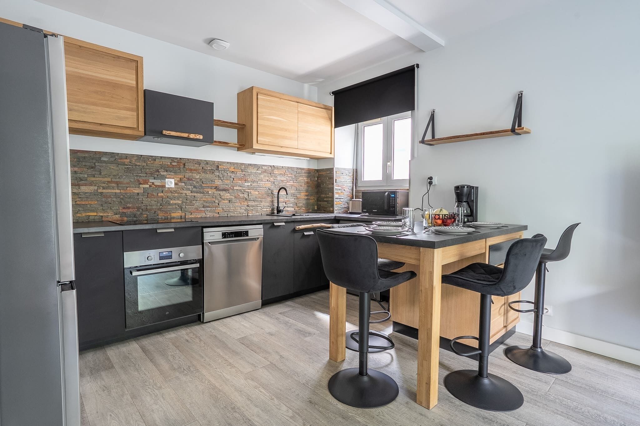 Een moderne keuken met een centraal eiland, zwarte barkrukken en een inbouwoven.