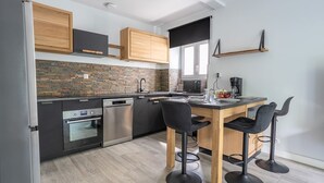 A modern kitchen with a central island, black bar stools, and a built-in oven. - L’Escapade du Quai - Proche Gare (Pontivy)