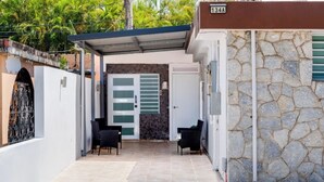 Un espacio al aire libre cubierto con un muro de piedra, una puerta con un diseño verde y blanco, y dos sillas negras.