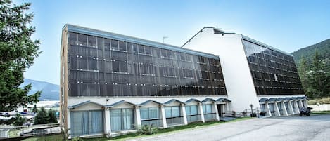 Un bâtiment moderne doté de grandes fenêtres et d’un toit plat, entouré d’un parking et d’espaces verts.
