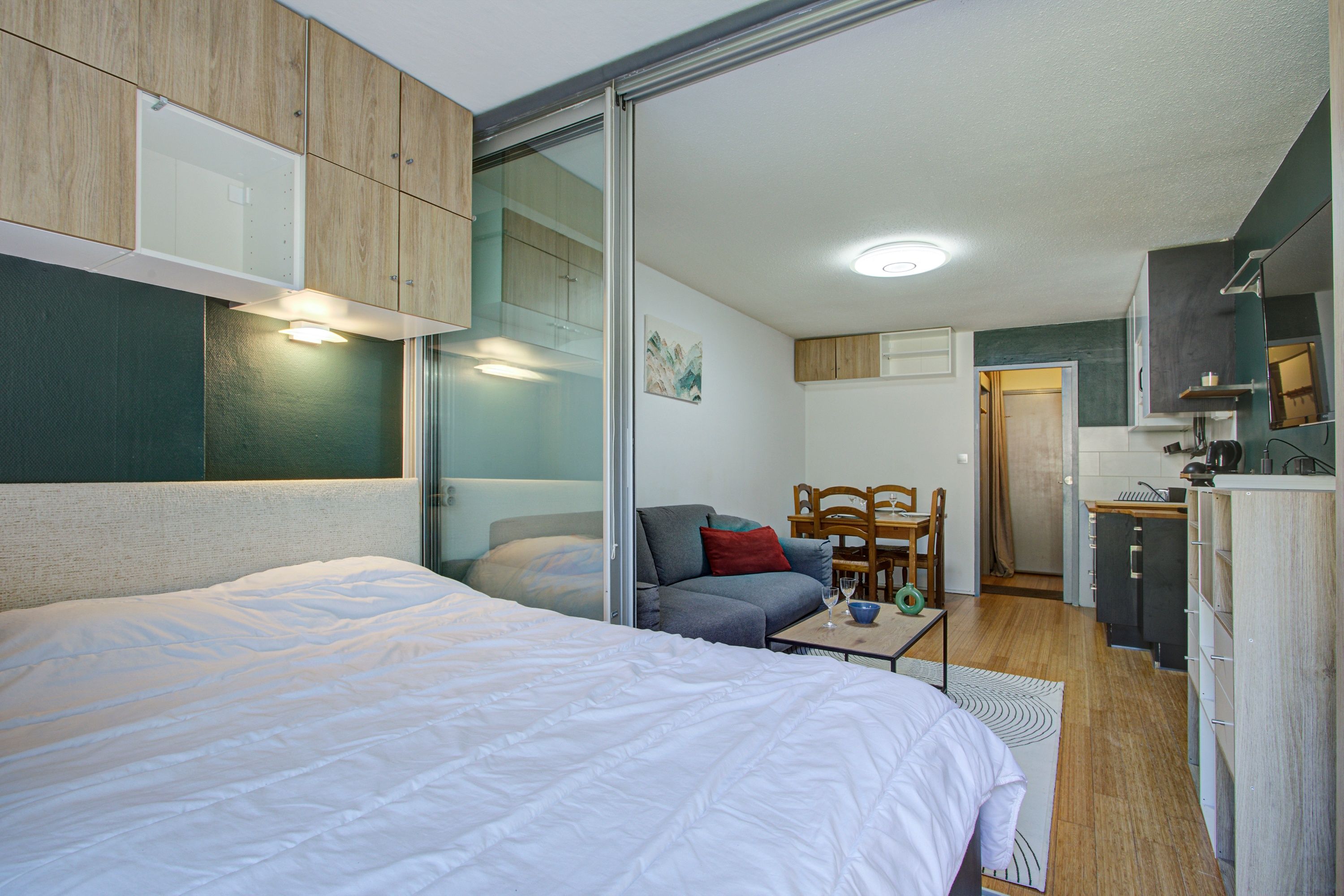A compact room with a bed, a sofa, a dining table, and a kitchenette.