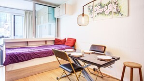 Una habitación pequeña con cama, mesa de comedor y sillas, y una ventana.