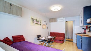 Una habitación compacta con cama, una pequeña mesa de comedor, un sofá y una kitchenette.