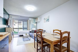 A modern, well-lit room with a dining table, chairs, a bed, and a view through a glass door.