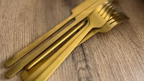 Une table en bois sur laquelle est posée une pile d’assiettes blanches et un ensemble de fourchettes de couleur dorée.