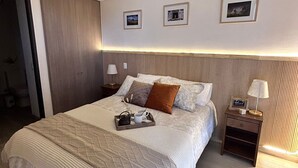 Une chambre à coucher moderne avec un grand lit, une tête de lit en bois, des tables de chevet et des tableaux encadrés accrochés au mur.