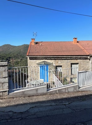 A stone building with a red-tiled roof, a blue door, and a small balcony with a white railing. - Village center house with terrace. (Zicavo)