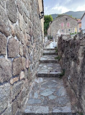 A stone staircase leading up a hill, flanked by stone walls, with a traditional building in the background. - Village center house with terrace. (Zicavo)