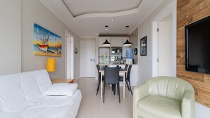 A modern living room with a white sofa, a green armchair, and a dining area with a table and chairs. - Apto com Vista mar em Canasvieiras Lbm401 (Florianópolis)