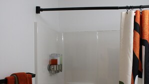 Una ducha con puerta de vidrio, un perchero con una toalla roja y una cortina de baño con estampado de hojas.