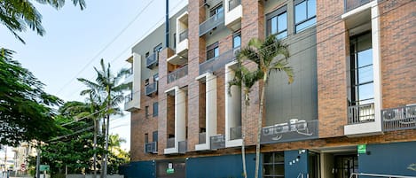 Un edificio de varios pisos con balcones, una entrada con portón y un letrero que indica 'SEU LUGAR FORA DE CASA' (hogar fuera de casa).