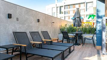 Un área de estar al aire libre moderna con sillones y mesas, una pequeña mesa con una silla y un paraguas decorativo.