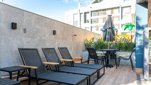 Eine Dachterrasse mit Liegestühlen, einem Tisch und Stühlen sowie einem grünen Sonnenschirm.