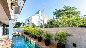 Un espace piscine moderne avec une terrasse en bois, entouré de plantes en pot et d’un mur en béton.