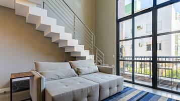 A modern living room with a sofa, a glass door leading to a balcony, and a staircase.