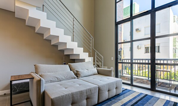 A modern living room with a sofa, a glass door leading to a balcony, and a staircase.