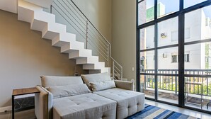 Un salon moderne avec un canapé, une porte vitrée donnant sur un balcon et un escalier.
