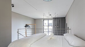 Une chambre d’hôtel moderne, équipée d’un lit, d’un luminaire suspendu et d’une fenêtre avec des rideaux.