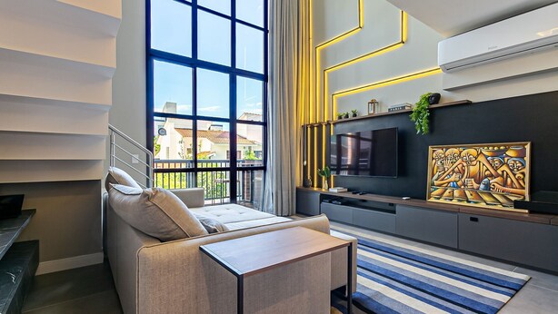 Un salon moderne avec une grande fenêtre, un canapé, un téléviseur et un élément décoratif mural.