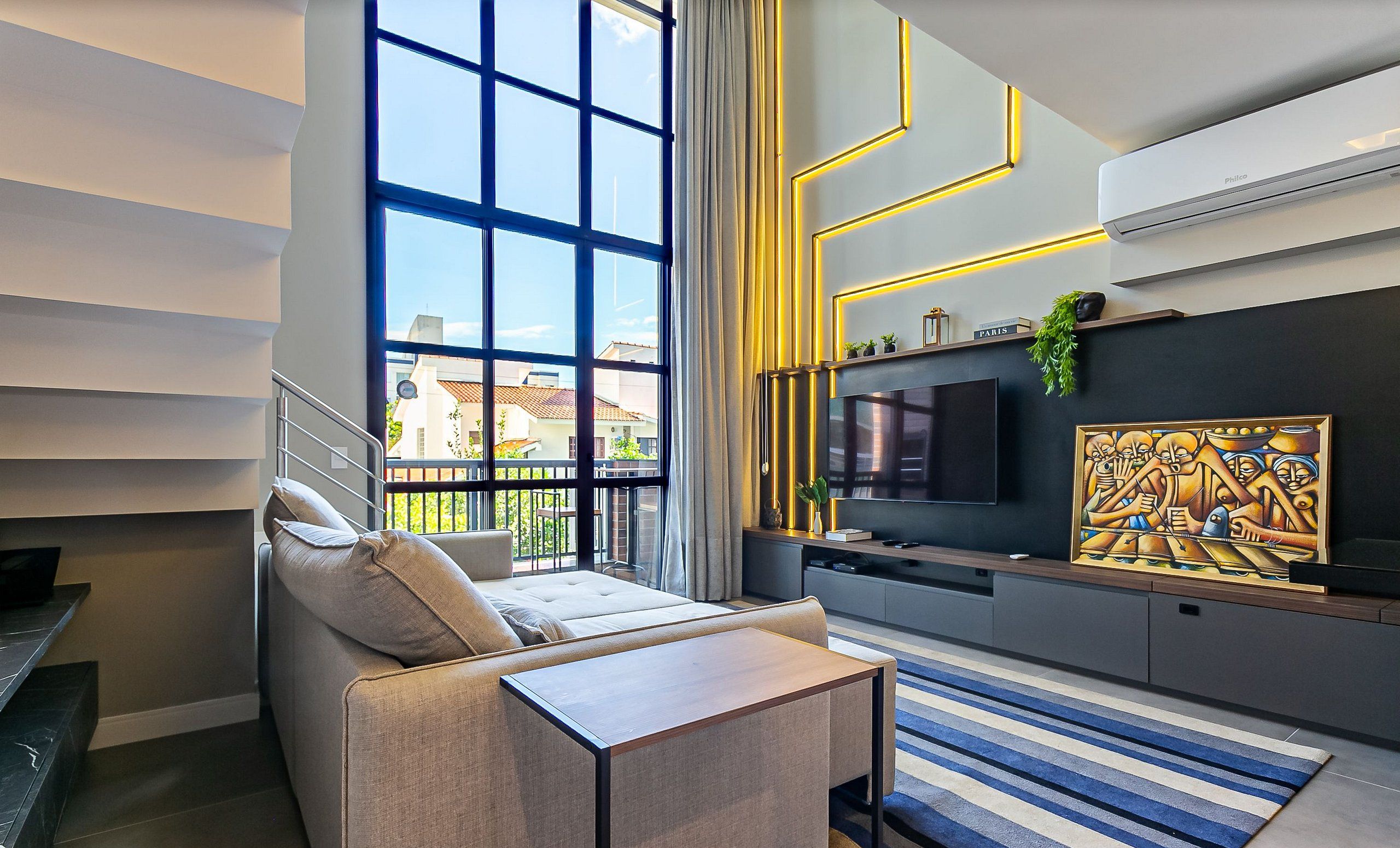 A modern living room with a large window, a sofa, a TV, and a decorative wall piece.