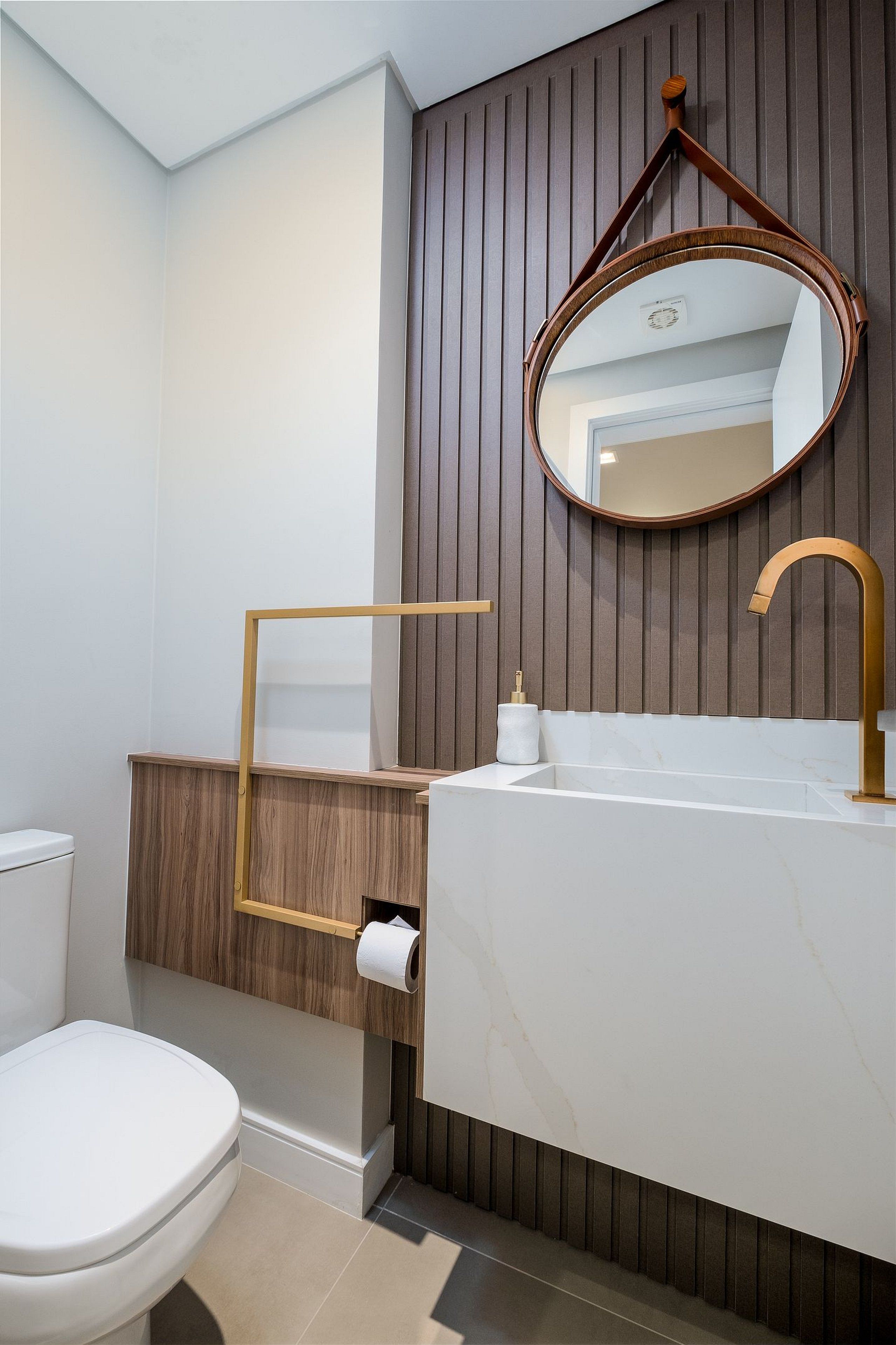 Et moderne badeværelse med et hvidt toilet, en trækommode, en marmorvask og et rundt spejl.