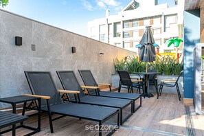 Een modern buitenzitgedeelte met loungestoelen en tafels, een kleine tafel met stoel, en een decoratieve parasol.