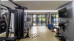 Un gimnasio con equipo de ejercicio, una banca y un televisor en la pared.