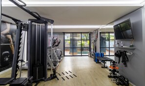 A gym with exercise equipment, a bench, and a TV on the wall.