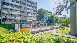 Ein Mehrfamilienhaus mit mehreren Etagen, einem Spielplatz mit verschiedenen Spielgeräten und einem gepflegten Garten.